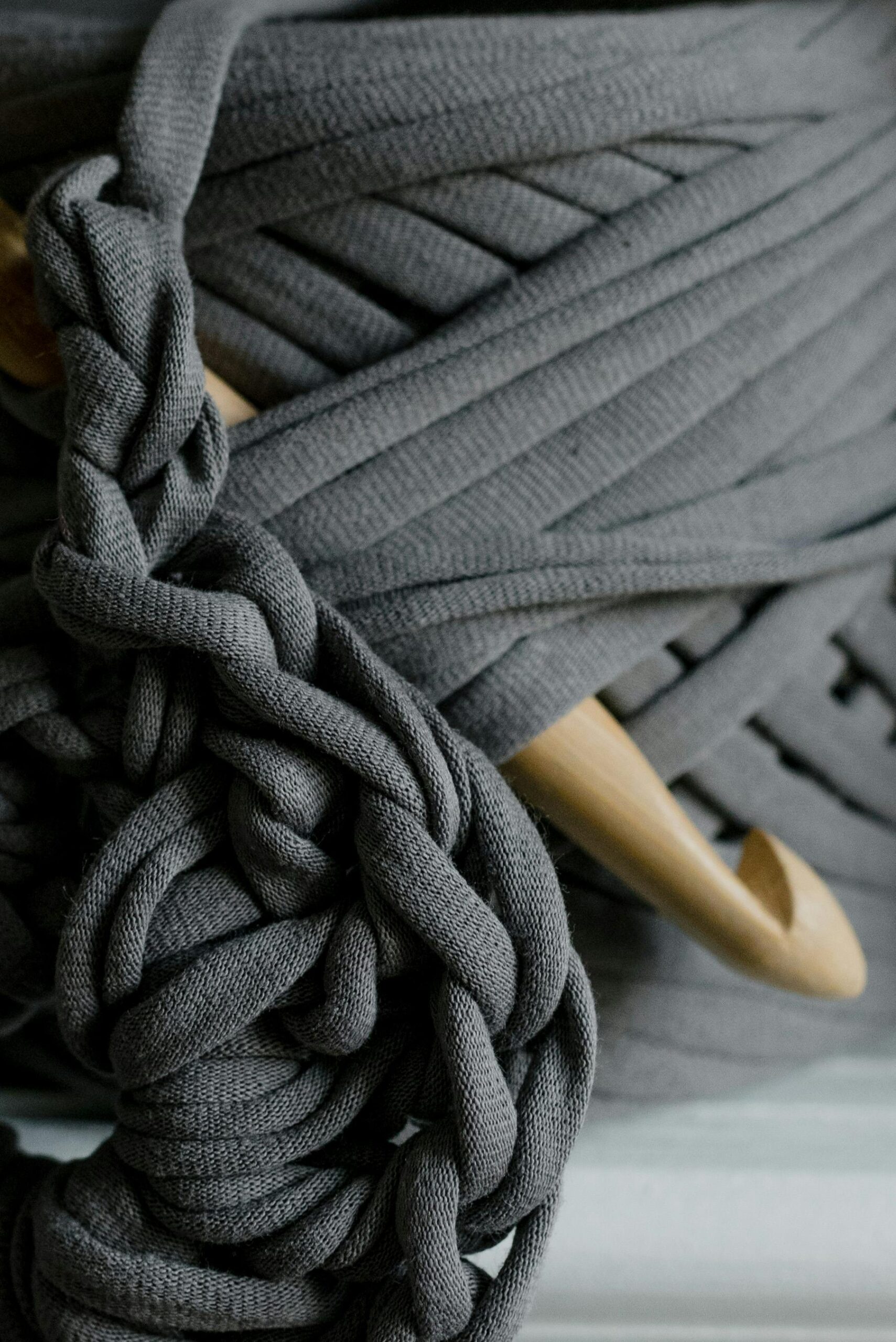 Detailed view of gray yarn with a wooden crochet hook, showcasing the art of crochet work.